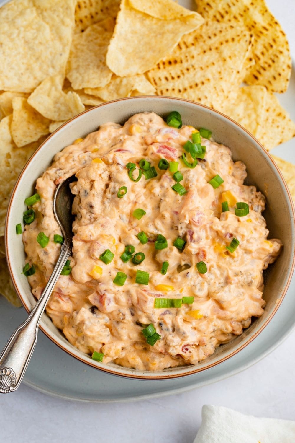 Bowl of cheesy cowboy crack dip with corn, onions and chips.