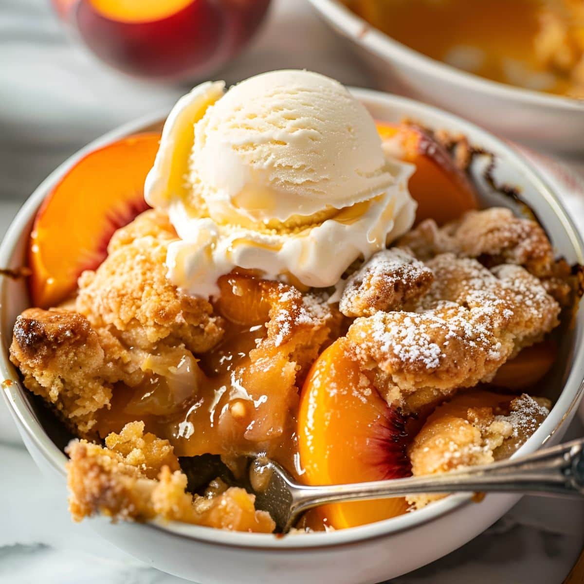 Cake Mix Cobbler with Peaches in a Serving Bowl with Vanilla Ice Cream and a Spoon