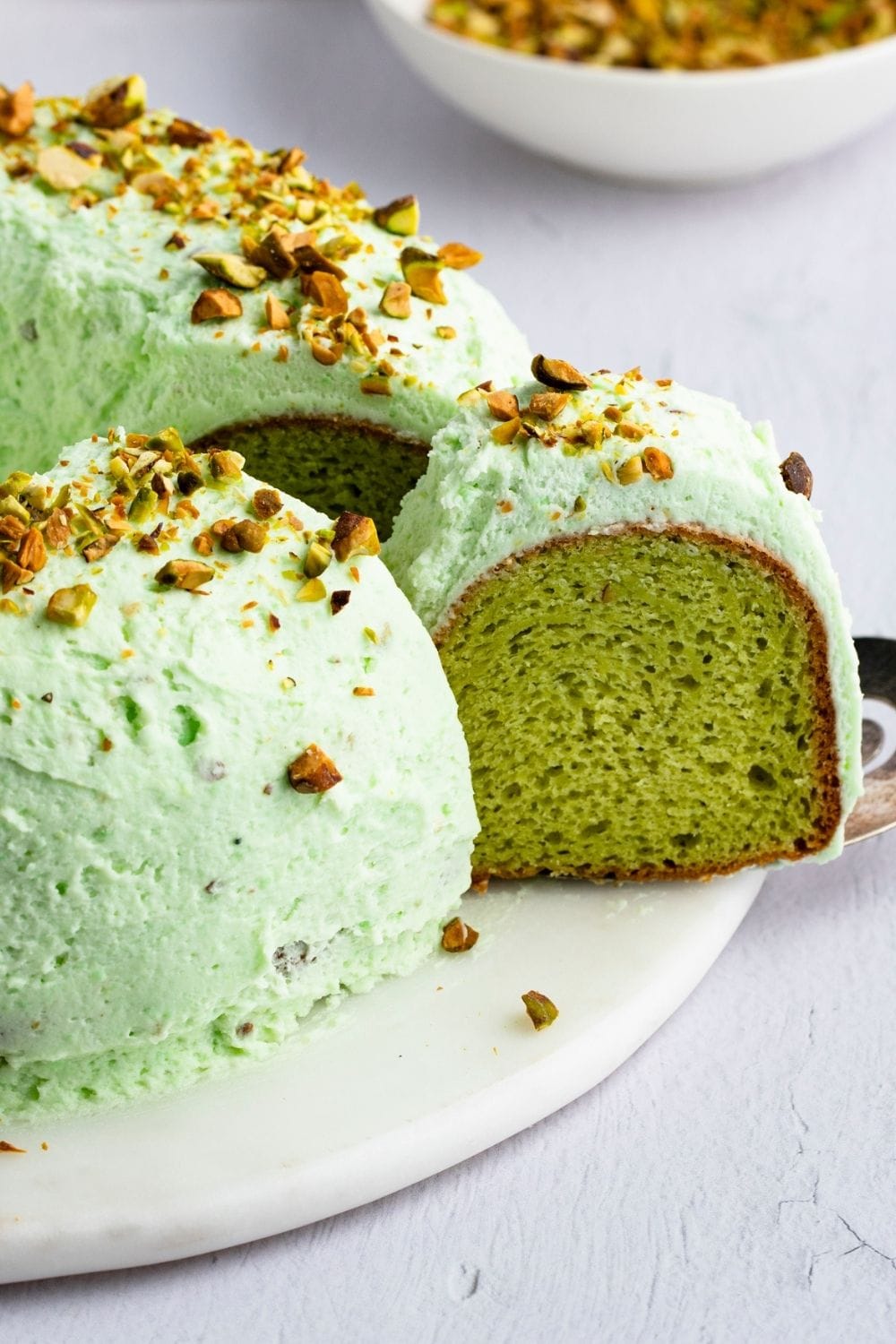 Sliced pistachio cake with green frosting topped with chopped pecans. 