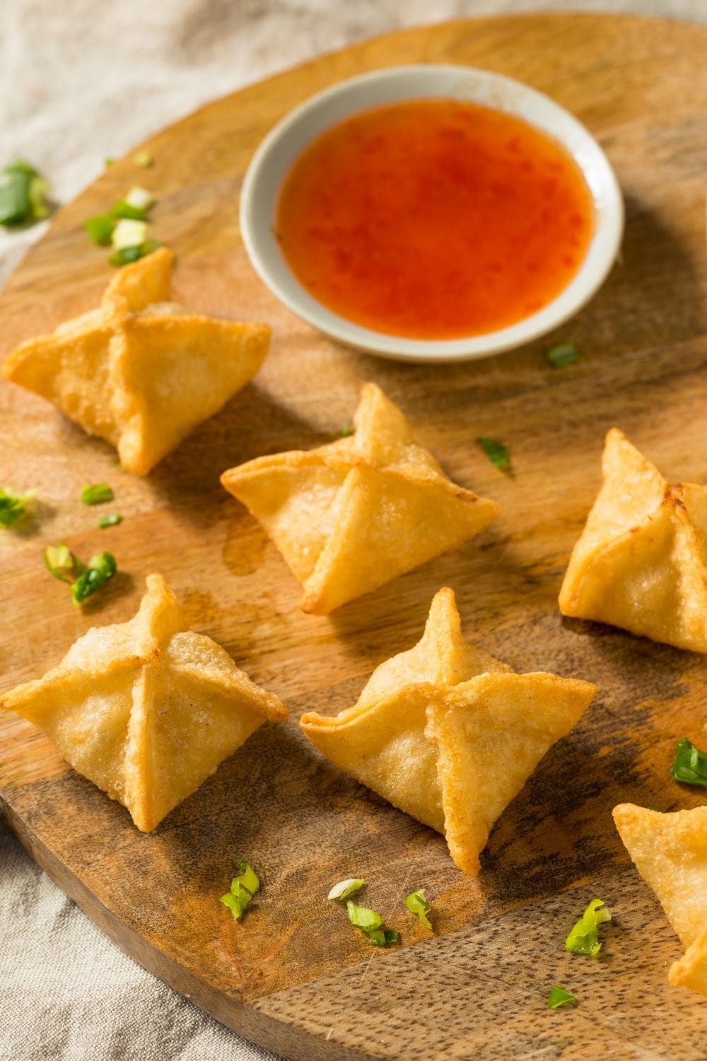 Air flyer crab Rangoon arranged on a wooden cutting board with sweet and sour dip.  
