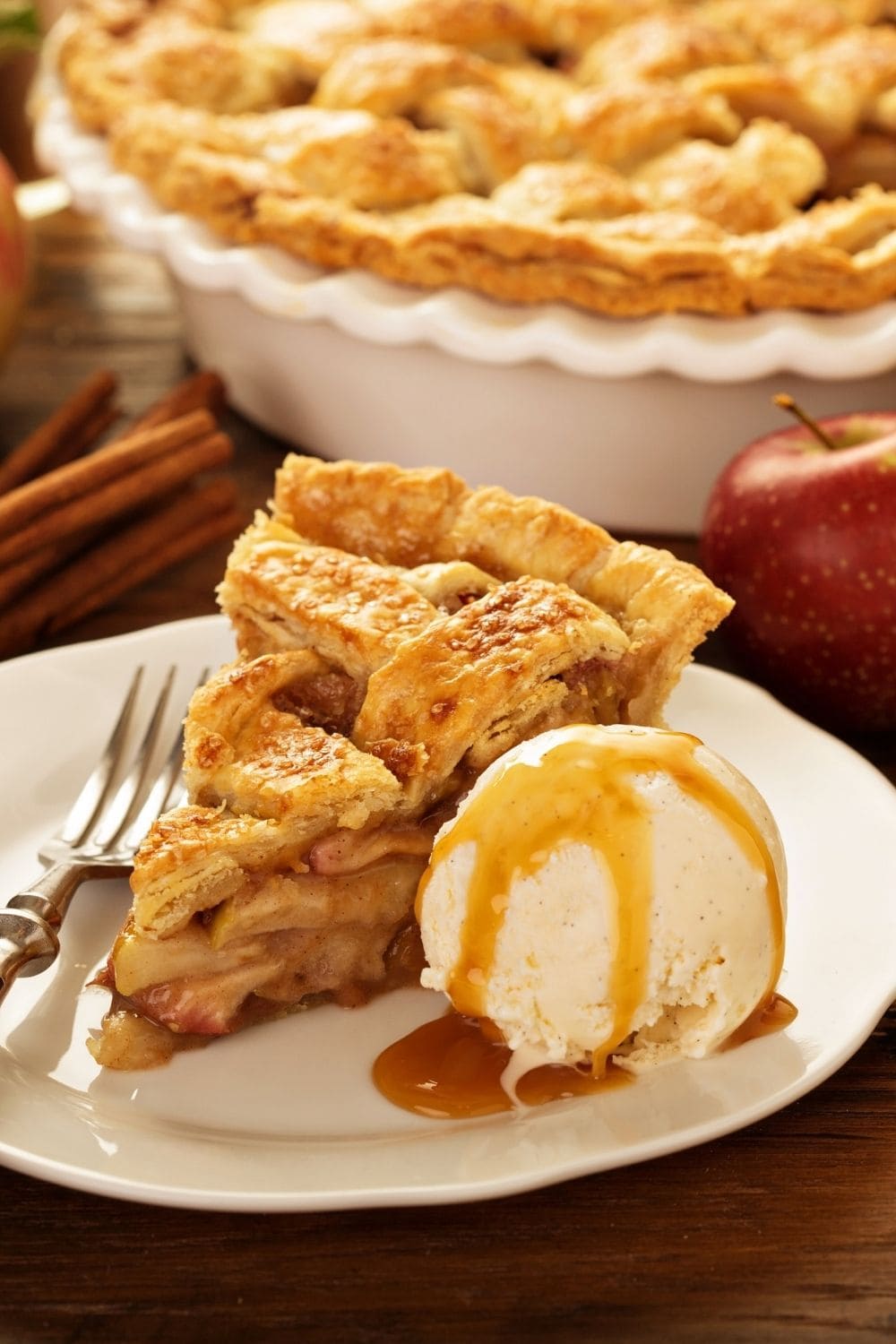 A slice of apple pie served with a scoop of vanilla drizzled with caramel syrup on top.