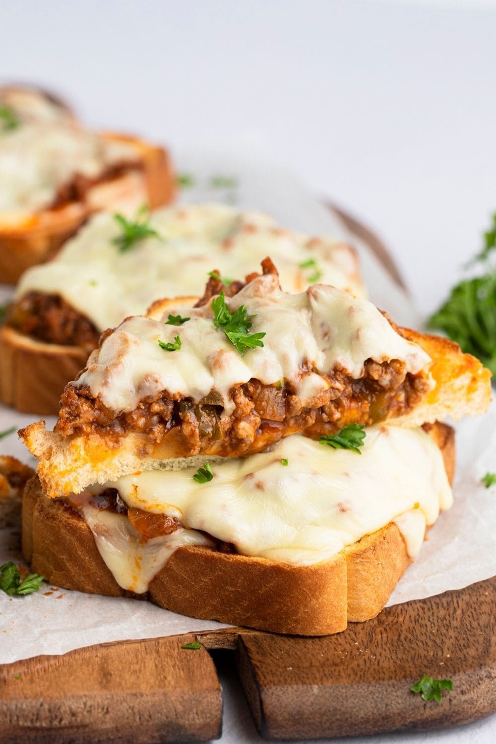 Open-faced sandwiches with saucy ground beef filling with onion and bell peppers topped with American cheese served on a wooden cutting board with parchment paper