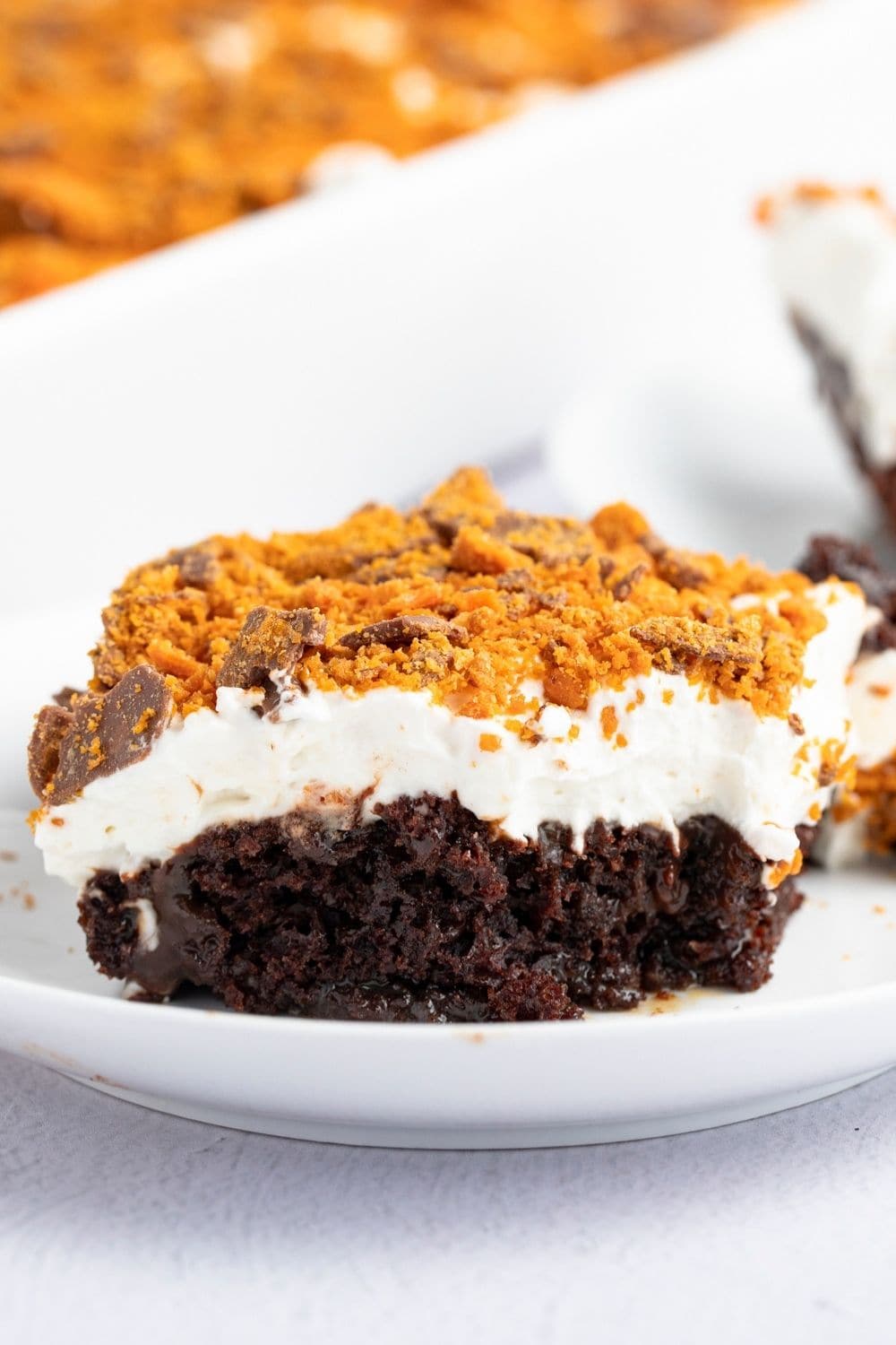 Slice of Butterfinger Cake with cool whip, caramel, hot fudge, and crushed Butterfinger candy on top