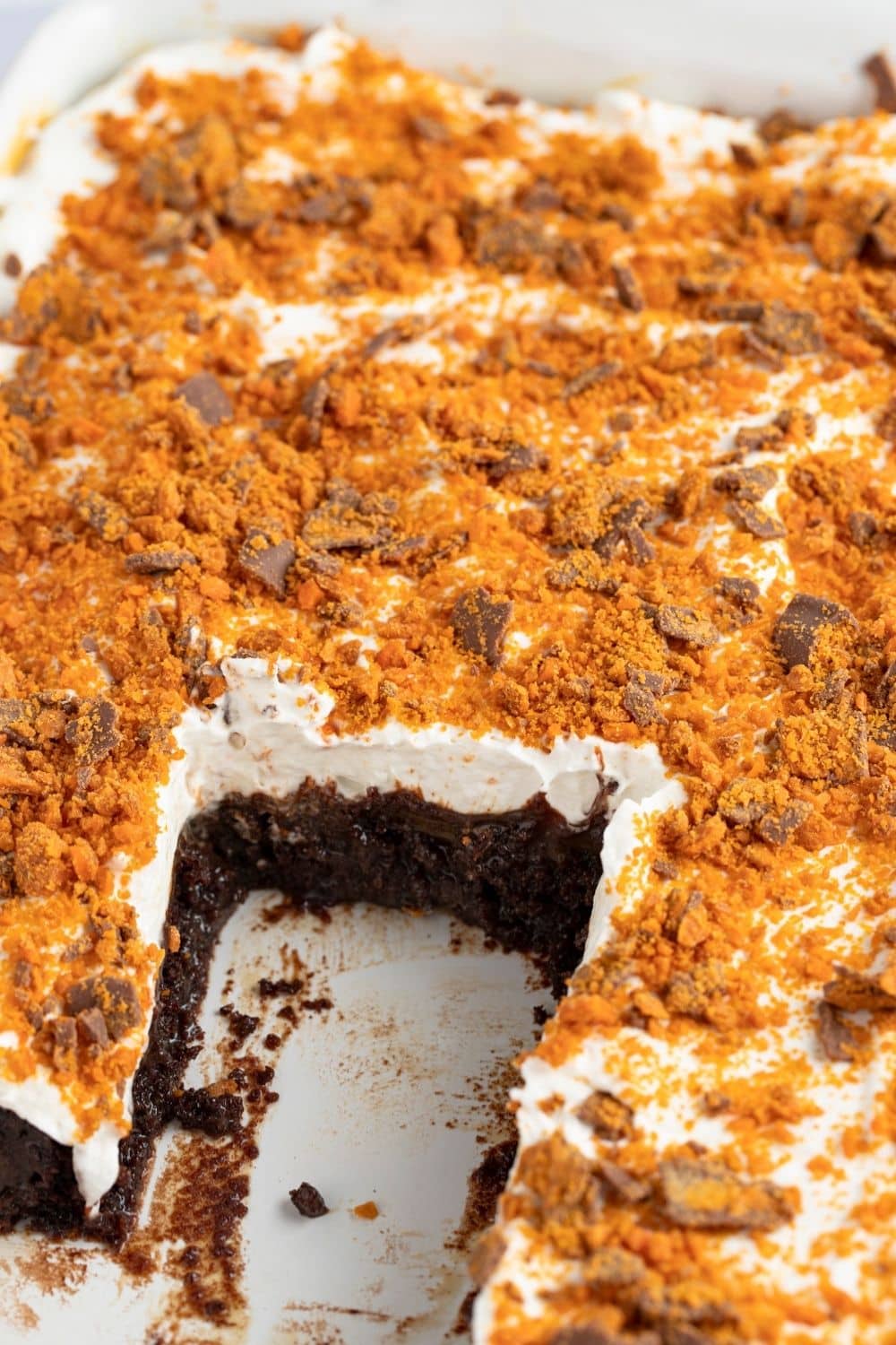 Close-up of the entire Butterfinger Cake with a few slices removed. The inner layer is ooey gooey with with moist chocolate cake, cool whip, caramel, hot fudge, and crushed Butterfinger candy on top
