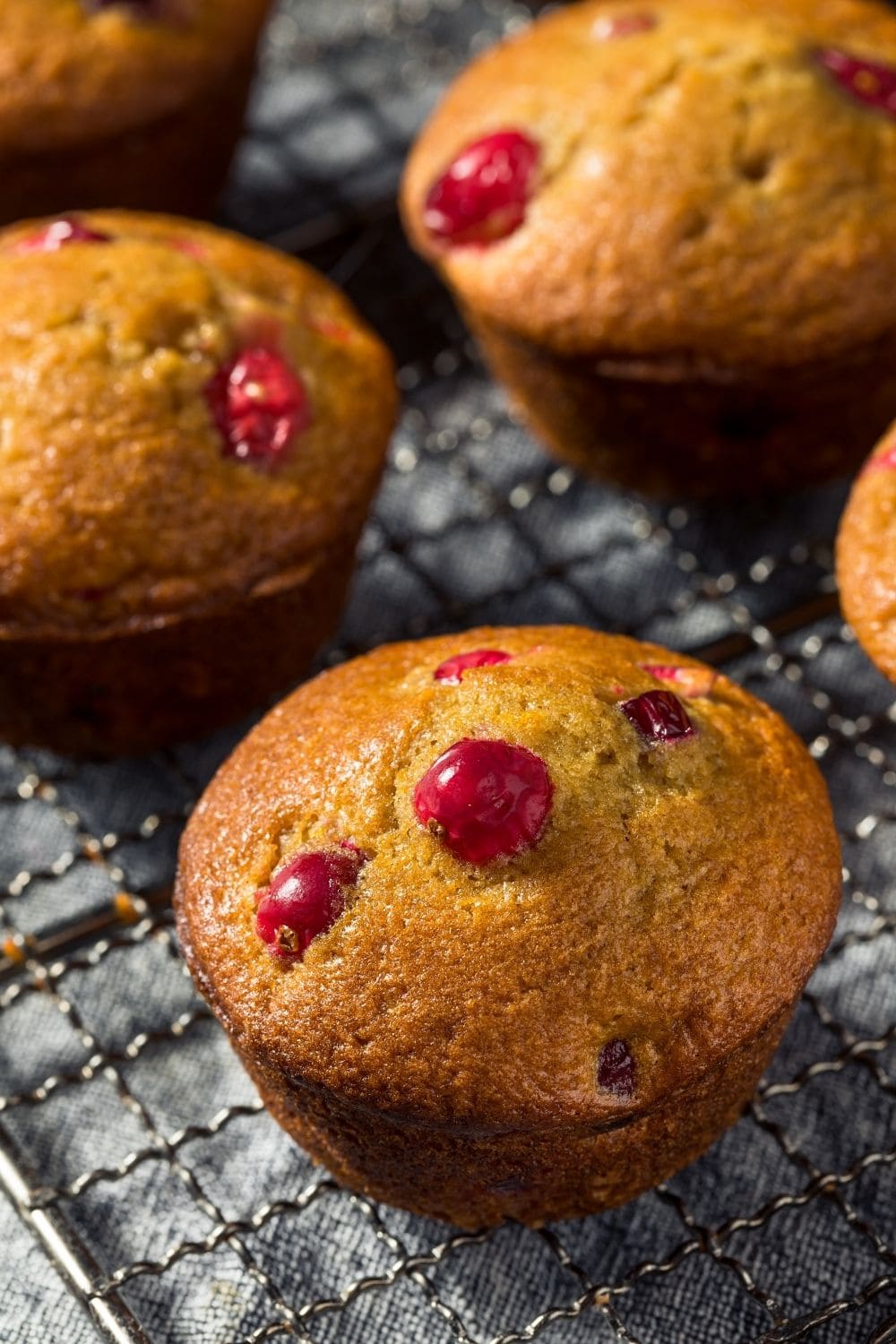 Orange muffins with cranberries on a cooling rack. 