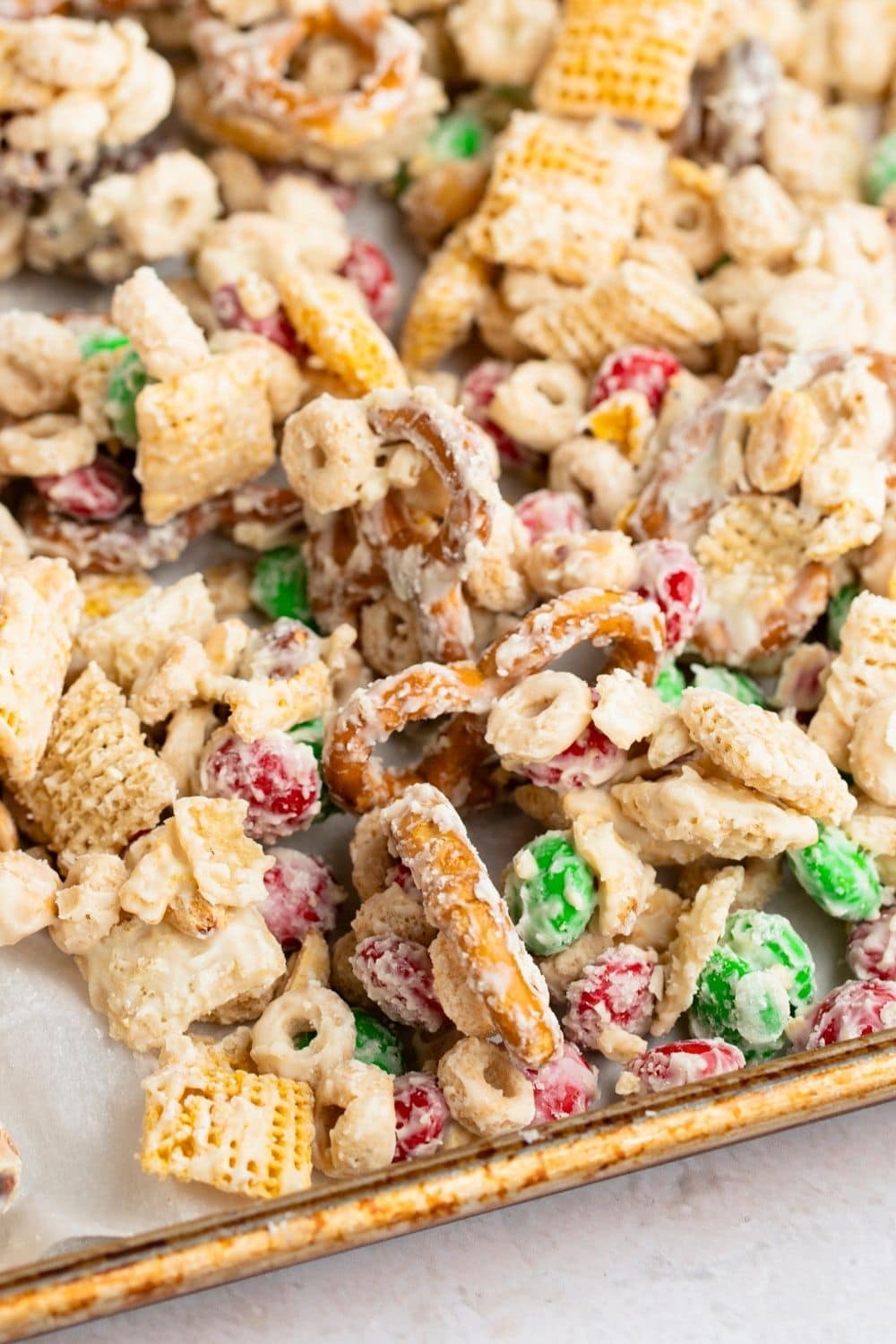 Chex mix, nuts, pretzels, and M&M candies, all coated in smooth, melting white chocolate served on a baking tray.