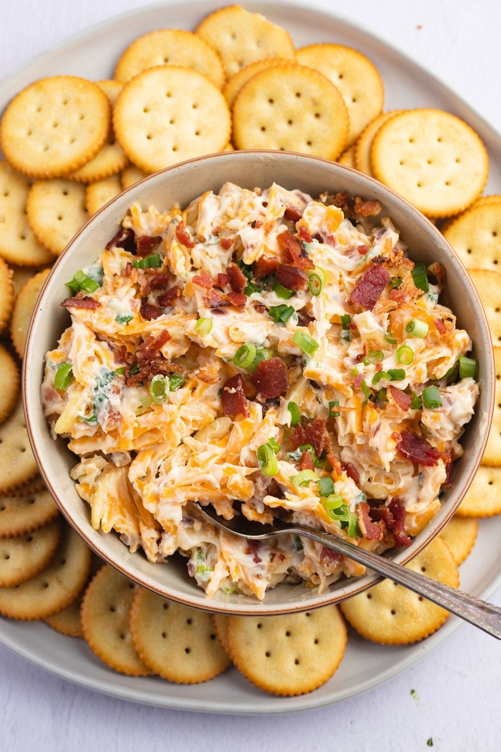 Dip made with mix of mayo, sharp cheddar, bacon, almonds, and green onion served on a bowl with a plate of crackers