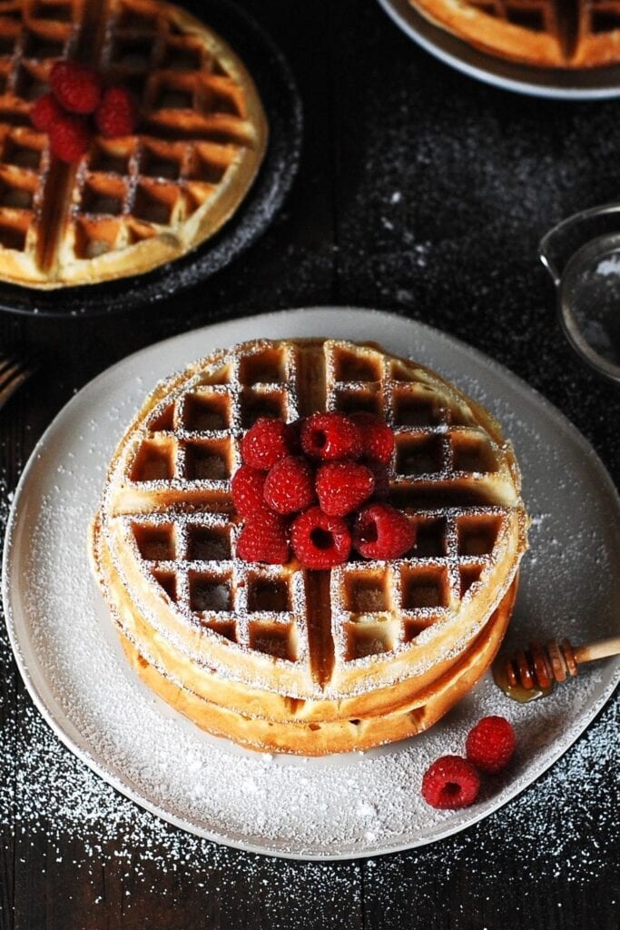 Thick and Fluffy Waffles with Berries and Powdered Sugar on a plate with honey
