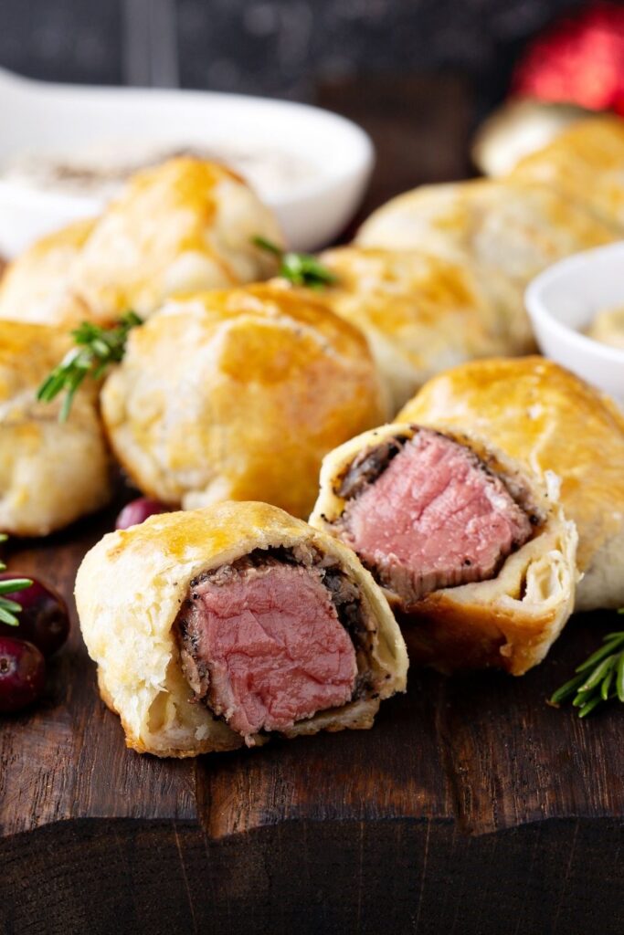 Easy Steak Appetizers To Wow Your Guests featuring Mini Beef Wellington Steak Bites served on a wooden board