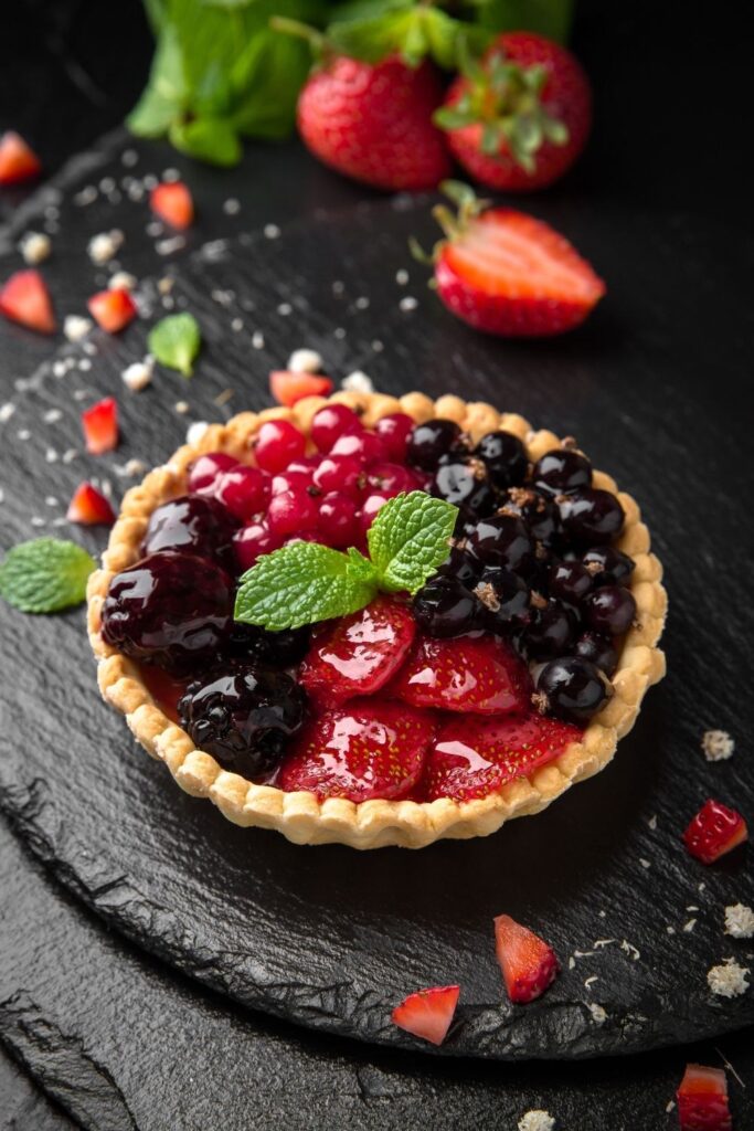 30 Sweet and Savory Tart Recipes That Are Easy and Tasty featuring a Homemade Sweet Berry Tart on a black slate with fresh mint