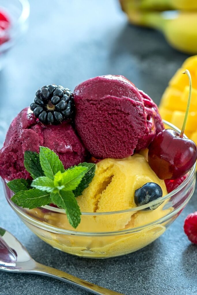10 Easy Sorbet Recipes (How To Make Sorbet at Home). Photo shows Sweet Blackberry and Mango Sorbet served in a glass bowl with fresh mint and blueberries