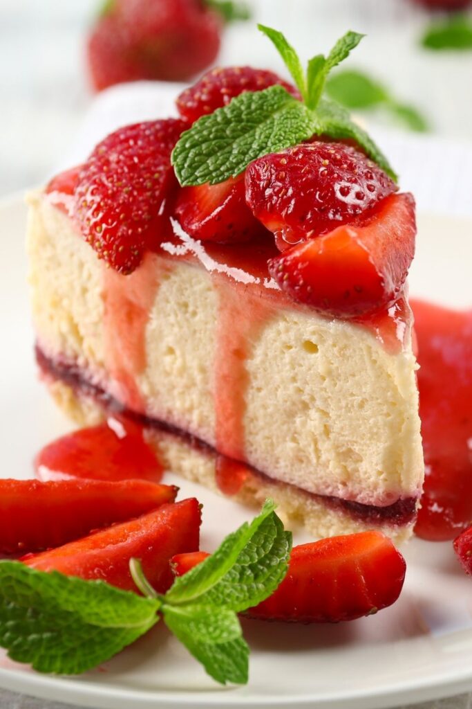 30 Best Cheesecake Recipes For The Most Indulgent Dessert. Photo shows Sweet Strawberry Cheesecake with Strawberry Sauce served on a plate with a mint leaf on top.