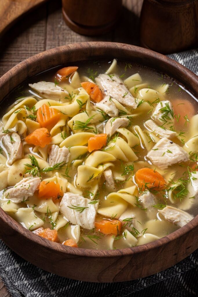 Cozy Rainy Day Recipes To Warm You Up featuring Warm Chicken Noodle Soup with Carrots served in a wooden bowl