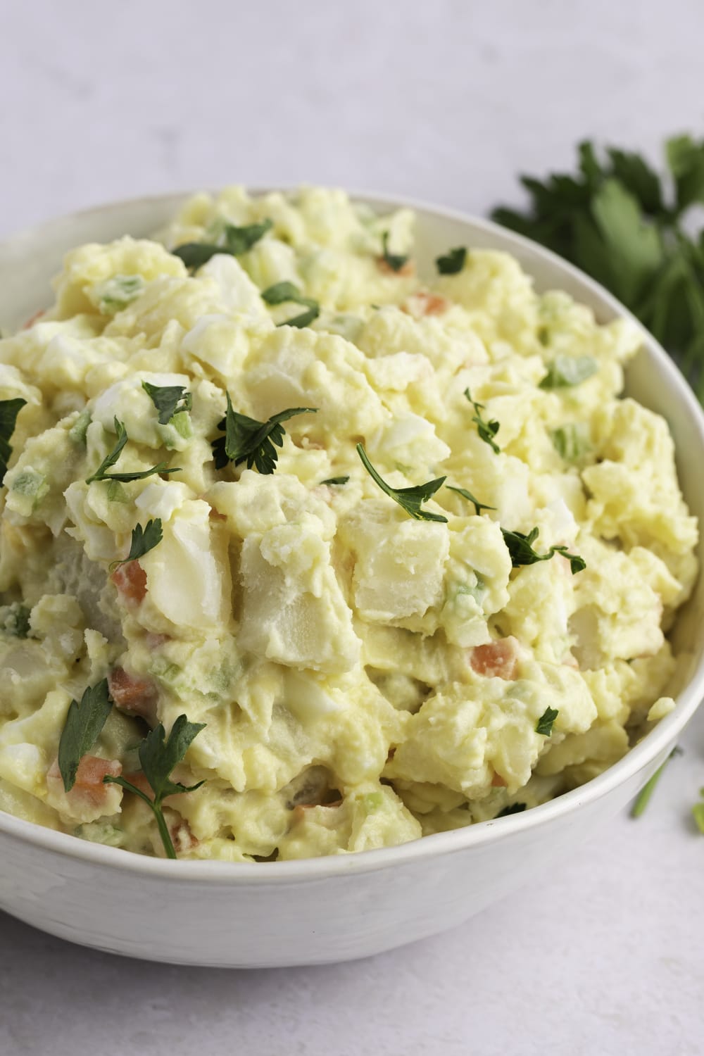 Potato salad garnished with chopped parsley served on a white bowl. 