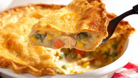 A slice of Campbell’s chicken pot pie being lifted from the dish, showing creamy chicken filling with peas, carrots, corn, and green beans under a golden, flaky crust.