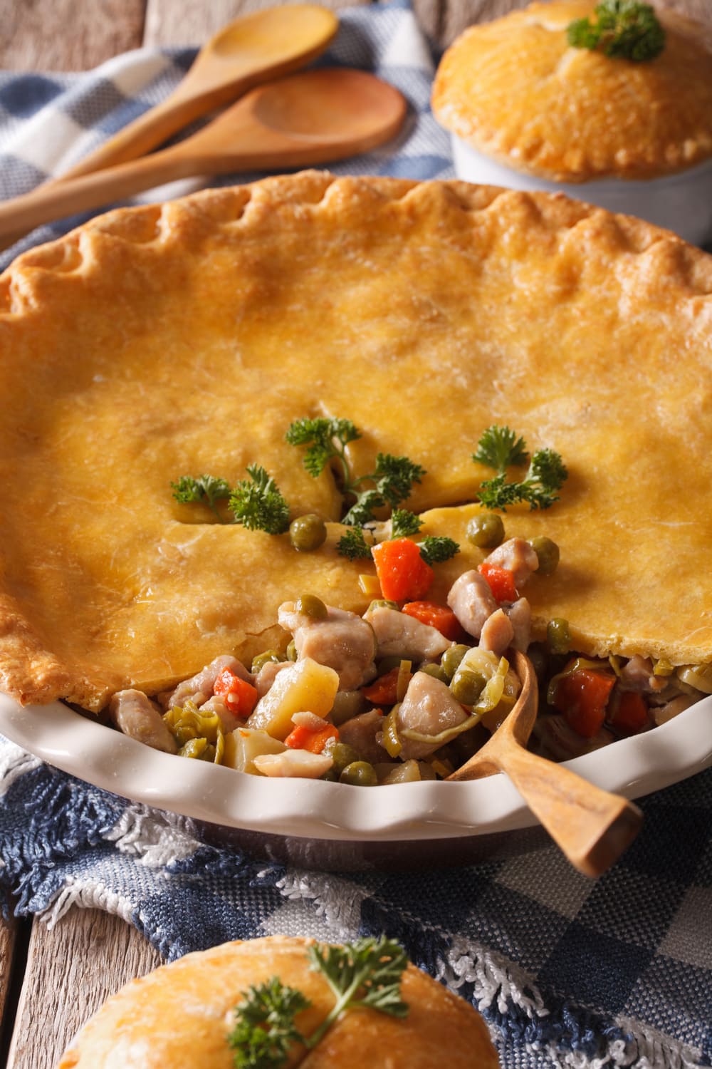 A savory pie filled with chicken, vegetables, and aromatic herbs with wooden spoon dipped on it.
