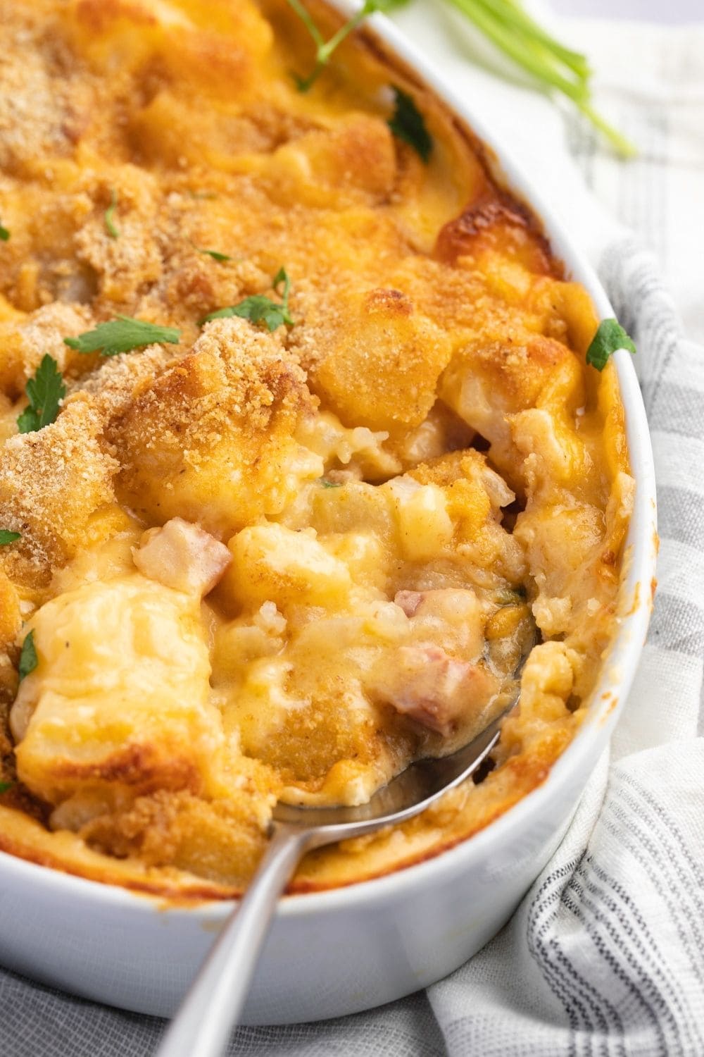 Ham and potatoes, smothered in melty cheese and creamy sauce, with a breadcrumb crust on top on a casserole with spoon.