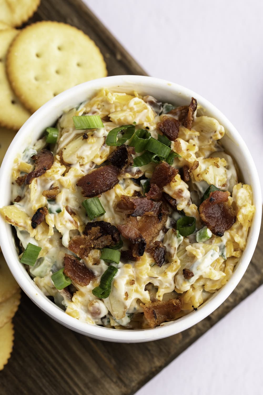 Cheesy dip in a bowl with toasted almonds, bacon crumbles, and cheddar cheese.