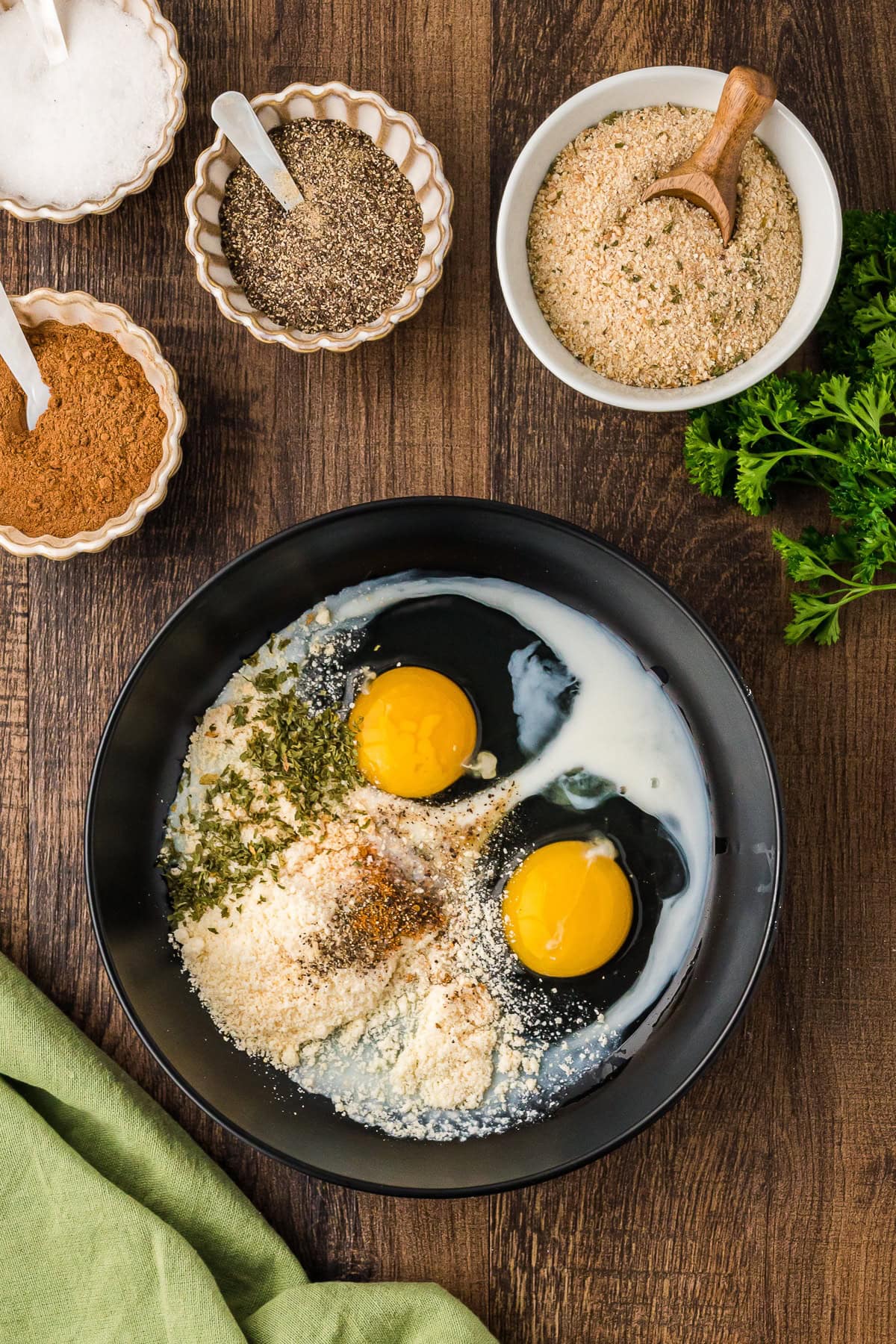 Eggs, breadcrumbs, flour and seasonings in a black bowl