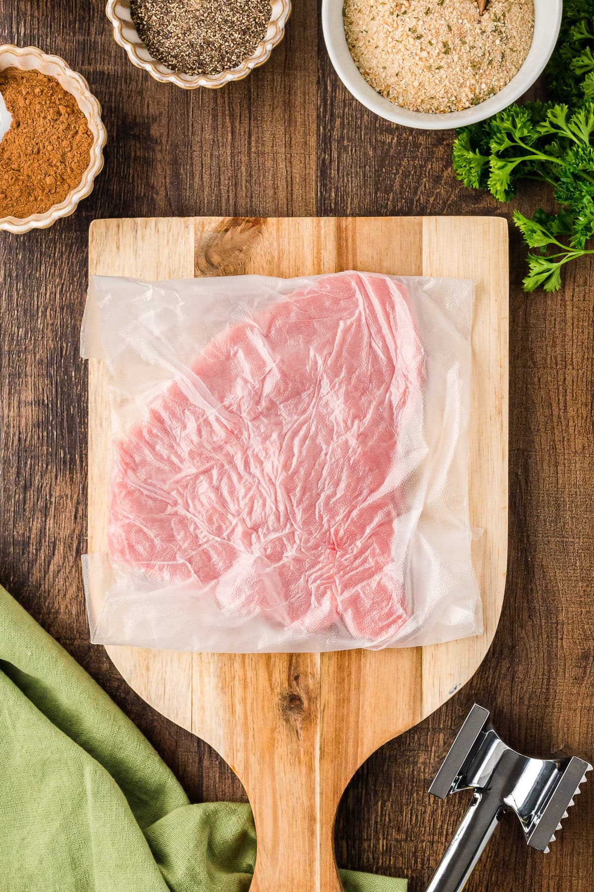 Veal cutlet covered with plastic on a wooden board, top view.