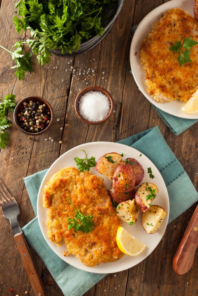 Wiener Schnitzel on Wooden Table with salt, peppercorns and roasted potatoes