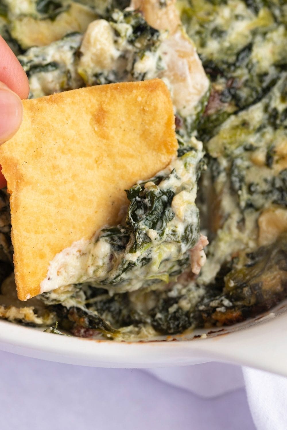 Chip dipped in creamy spinach artichoke dip on a bowl. 