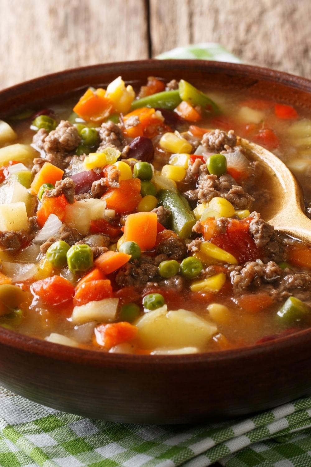 Old-fashioned Vegetable Beef Soup with Beef, Tomatoes, Peas, Carrots, Potatoes, Onions,  and Green Beans in a Bowl with a Wooden Spoon