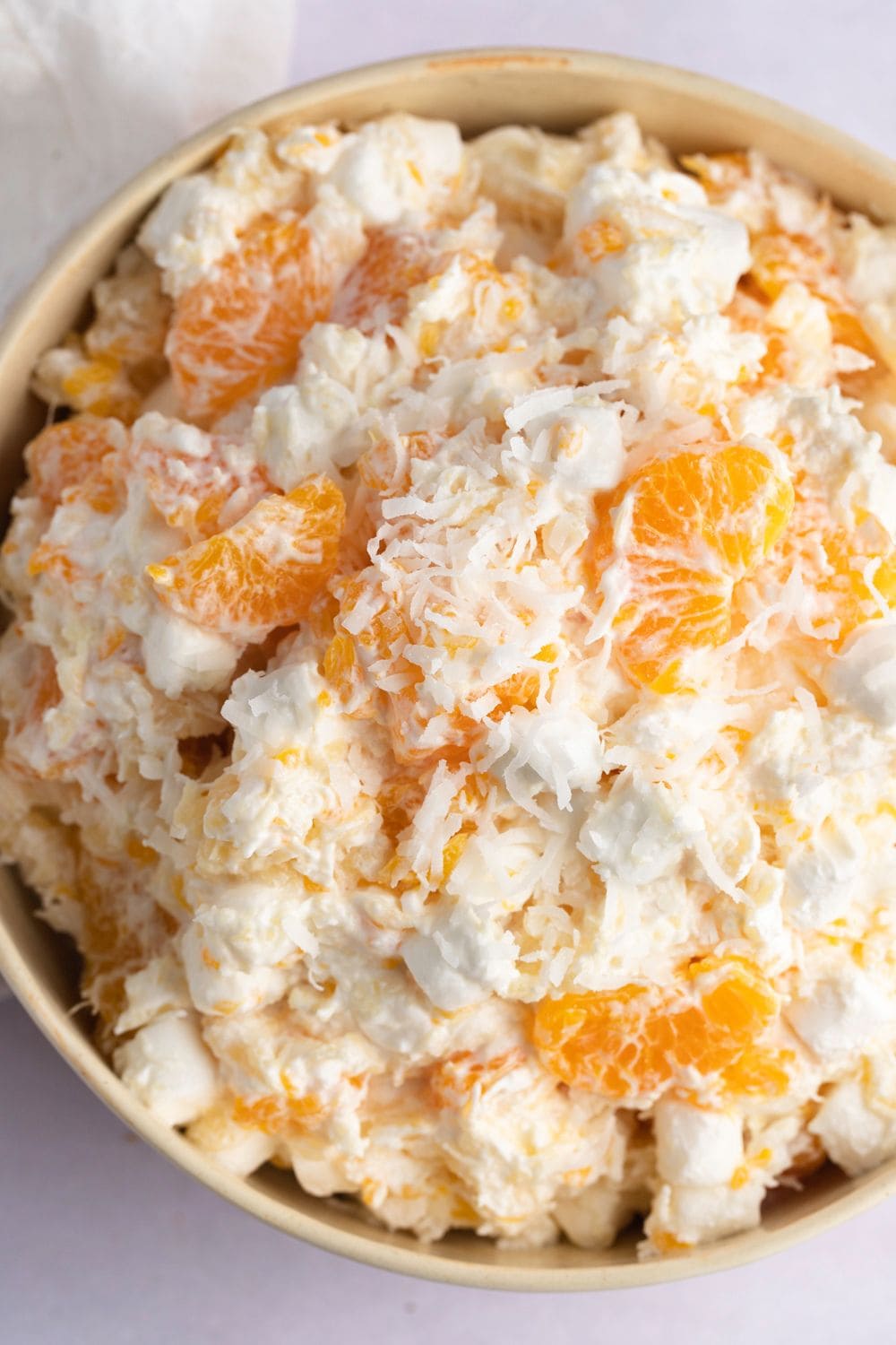 Bowl of salad made with crushed pineapple, mandarin oranges, whipped topping, marshmallows, and shredded coconut
