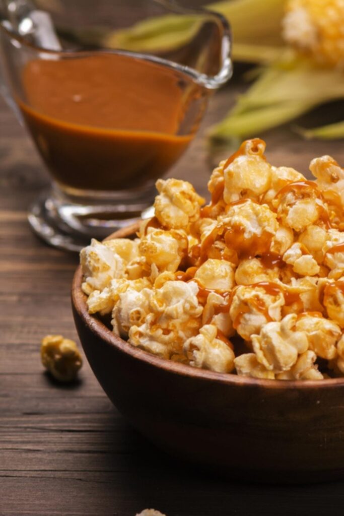 Popcorn in a bowl with a pitcher of caramel sauce