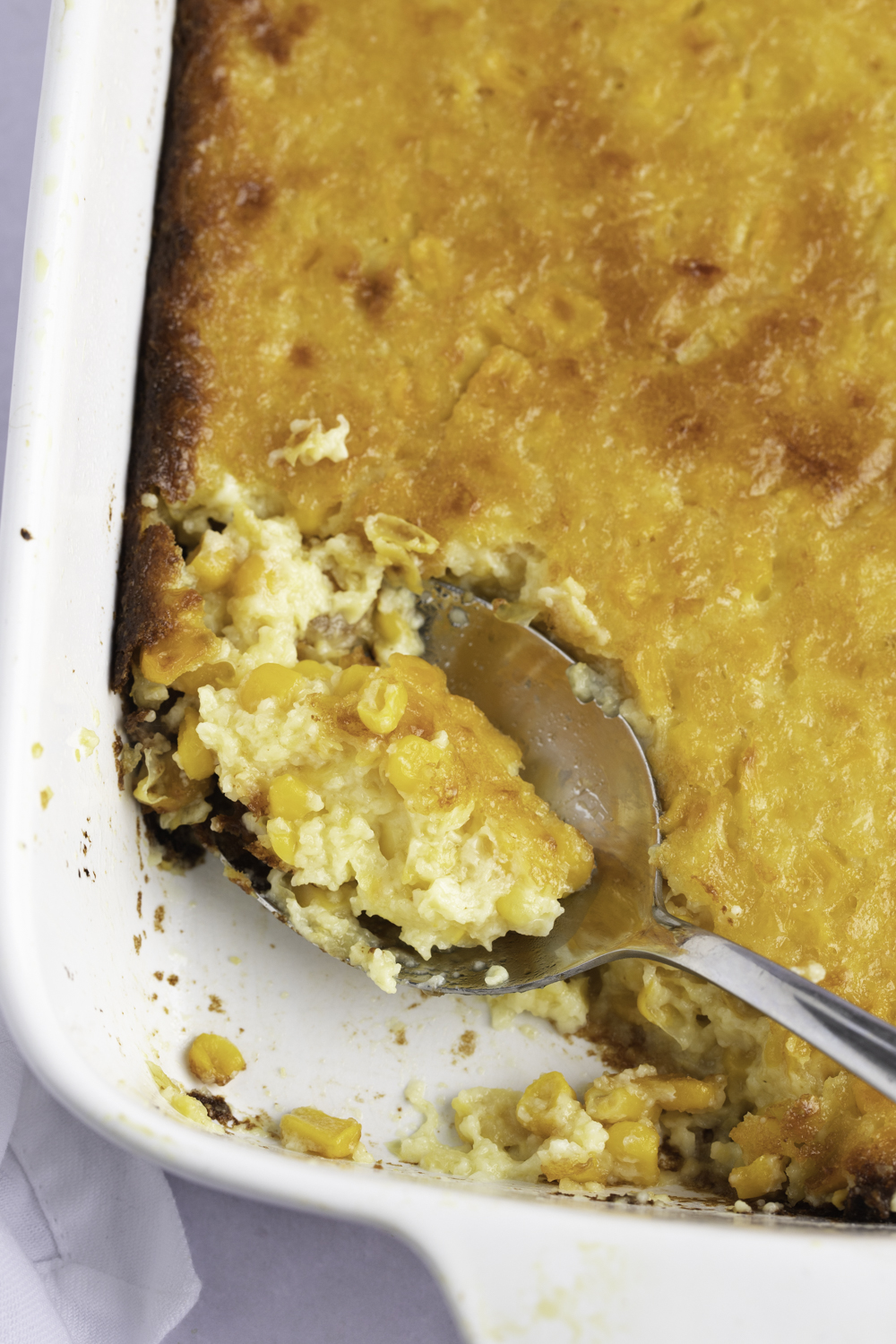 Spoonful of Creamy Corn Pudding scooped from a white dish. 