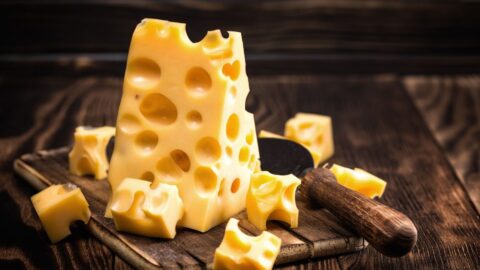 Gruyere Cheese with Big Holes and Knife in a Wooden Cutting Board
