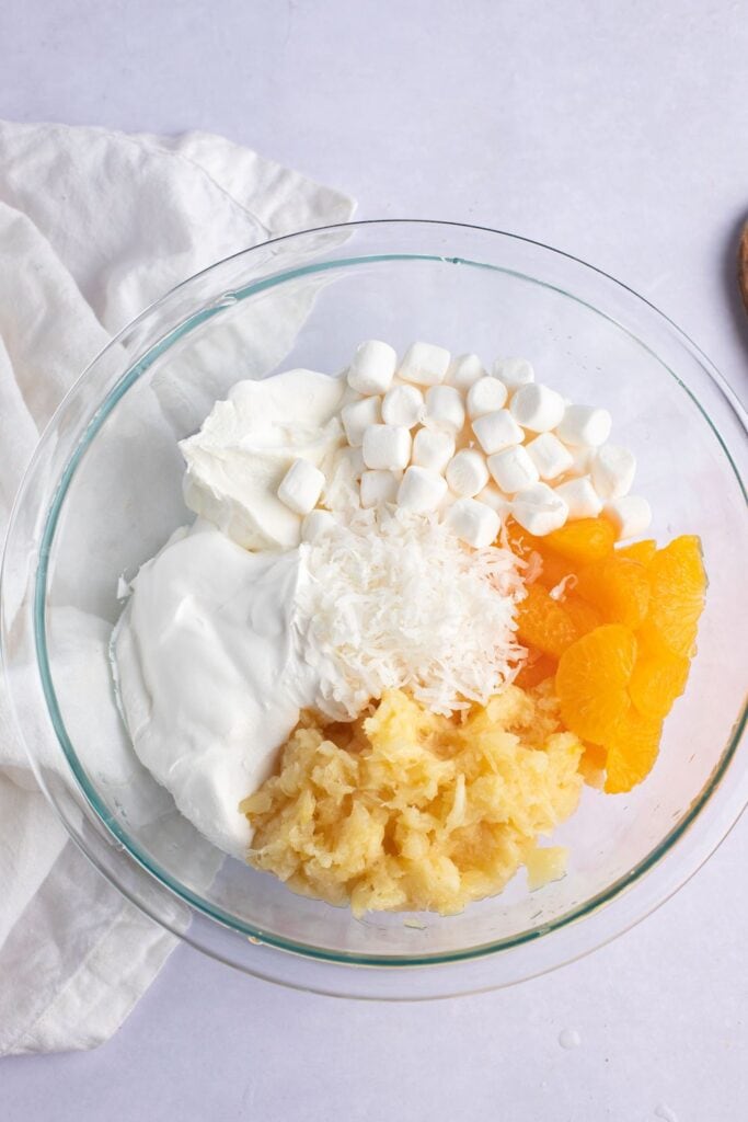 Mandarin Oranges, Pineapple Tidbits, Sour Cream, Shredded Coconuts and Mini Marshmallows in a Glass Bowl