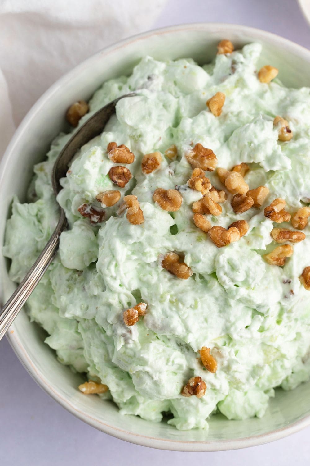 Watergate salad made with made with instant pudding mix, juicy pineapple, miniature marshmallows, and whipped cream, garnished with chopped pecans.