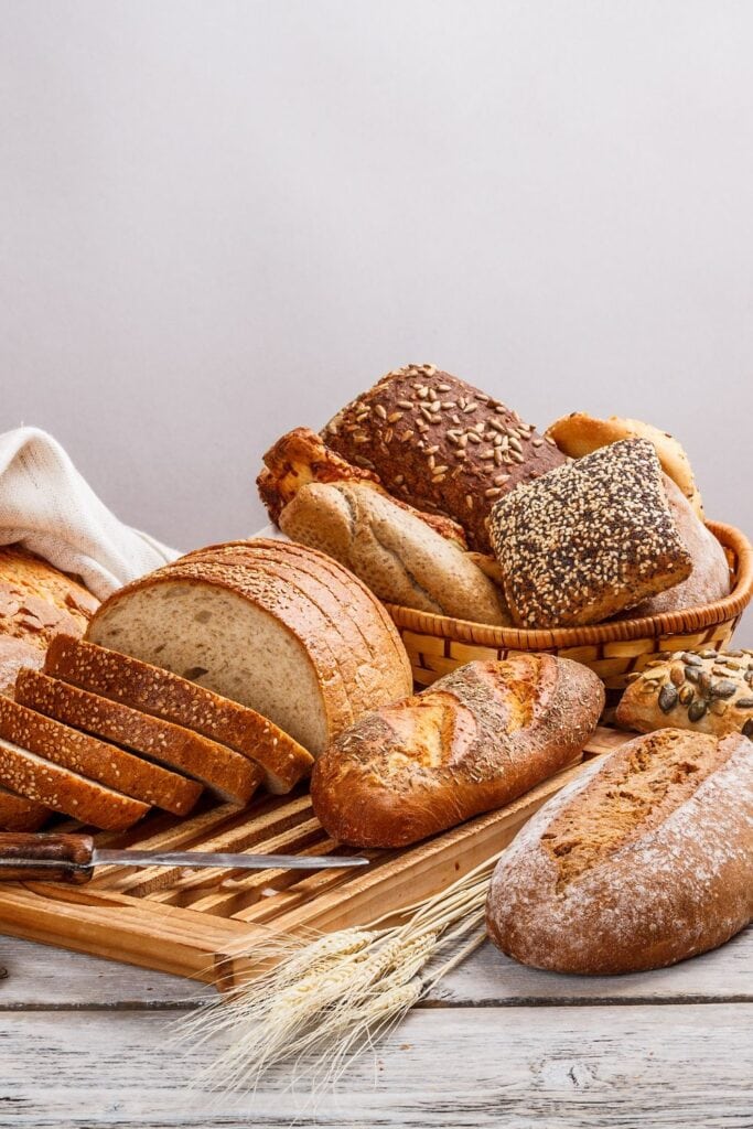 Assorted Bread in a Basket and Wooden Cutting Board