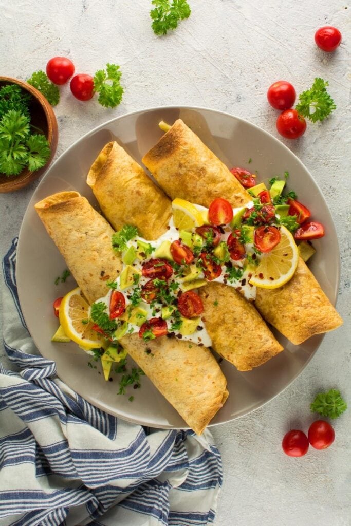 Vegan Pizza Taquitos on a Plate with tomatoes and lemon slices