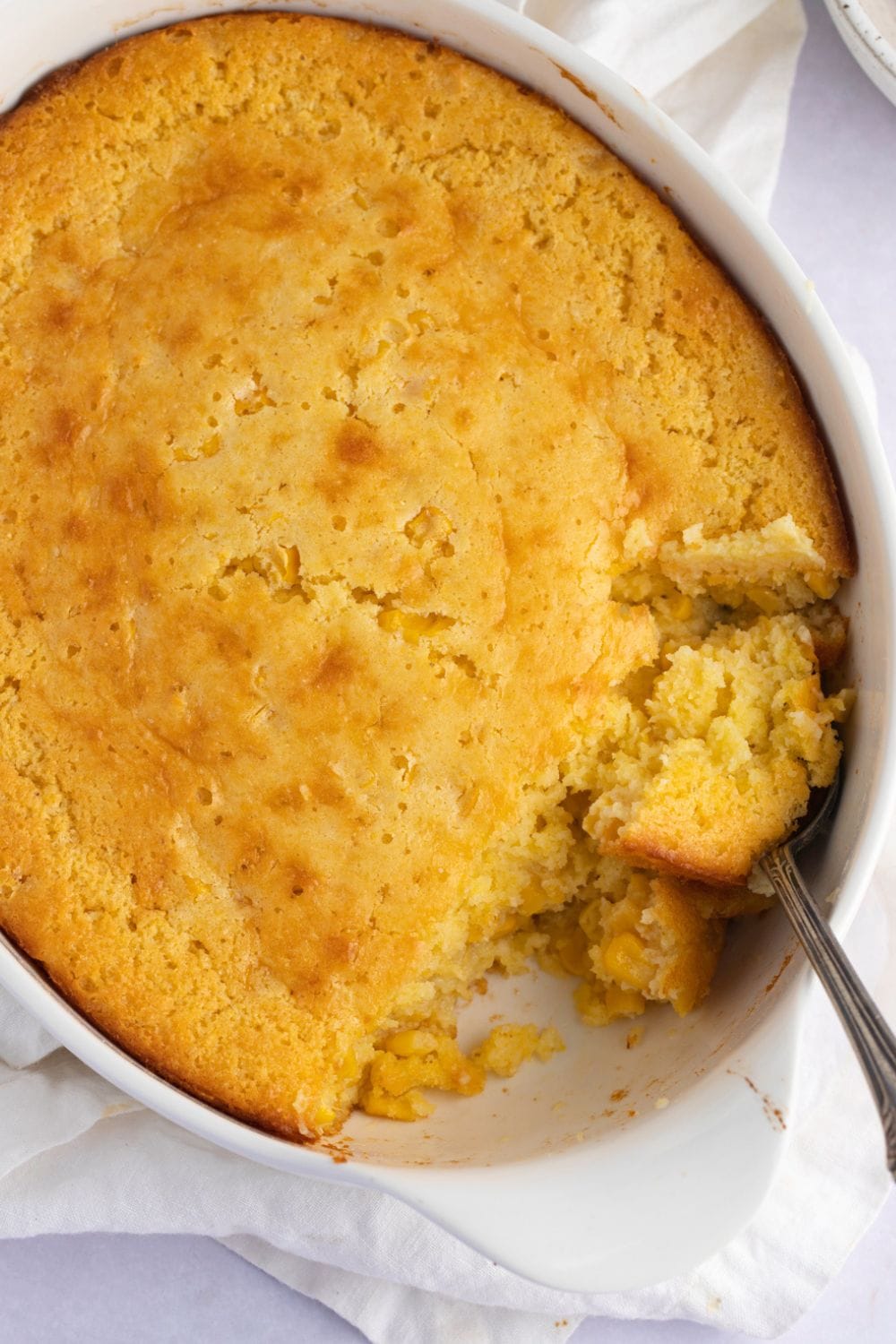 Cornbread casserole on a white baking dish with a spoon. 
