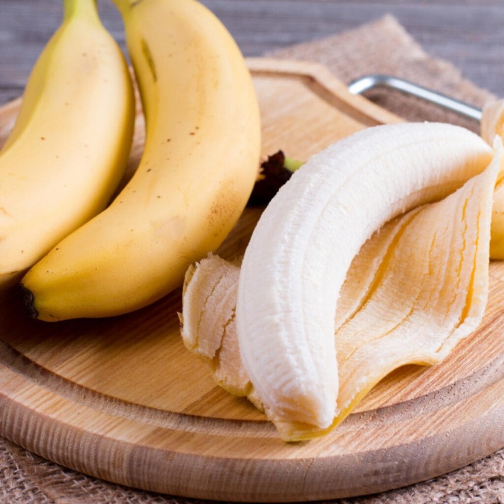 Banane sbucciate e non sbucciate su un tagliere di legno