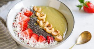 Bowl of Green Smoothie with Cashew Nuts, Coconut Flakes, Chia Seeds and Fresh Strawberries