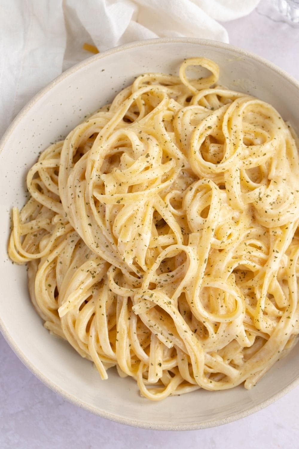 Pasta with creamy sauce sprinkled with dried herbs served on a white plate.