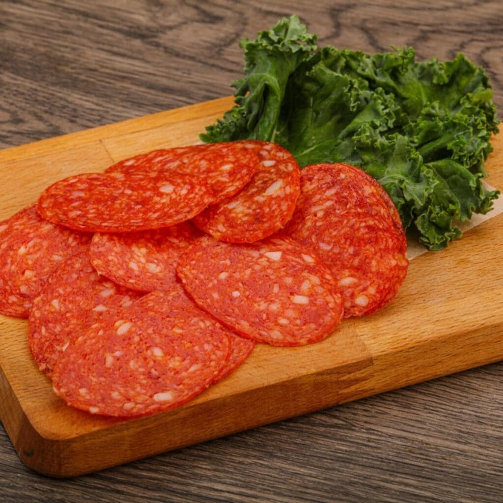 Pepperoni Slices on a Wooden Chopping Board with Lettuce Garnish