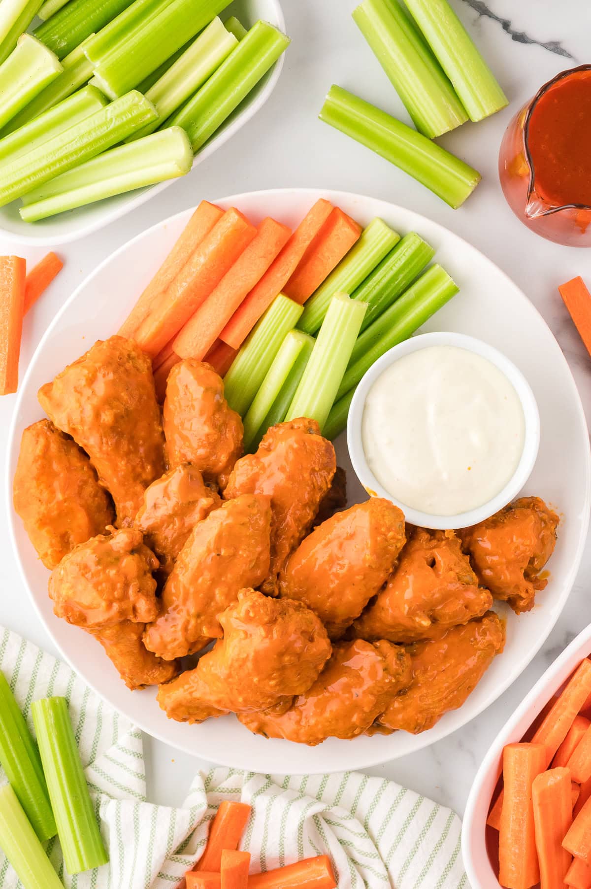 Crispy Buffalo Wings with ranch dressing, carrots, and celery sticks on the side served on a large white plate, top view
