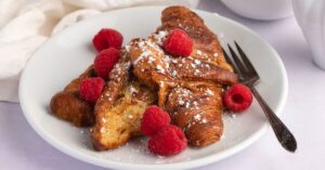 Buttery Homemade Croissant French Toast with Raspberries and Powdered Sugar for Breakfast