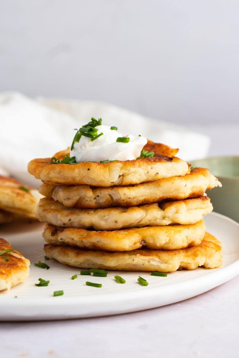 Pile of Potato Cakes Served on a White Plate With Sour Cream and Chives Garnish