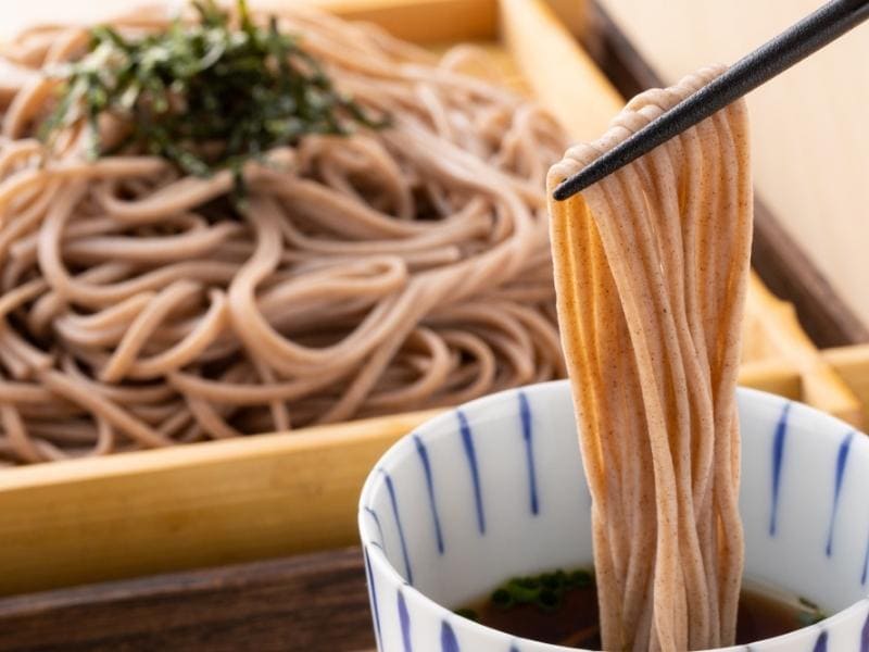 Soba Noodles Dipped Using a Wooden Chopsticks on a Flavored Dipping Sauce