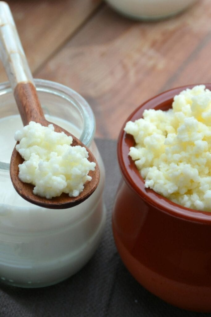 Yogurt on a Glass Jar and Kefir Scooped With a Wooden Spoon From a Brown Jar 