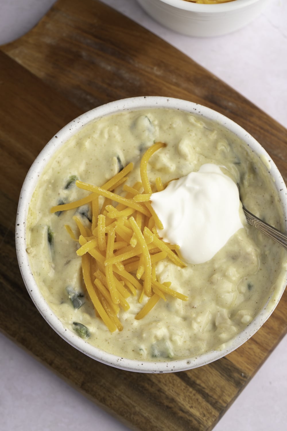 Green Chili Chicken Soup in a bowl topped with grated cheese and sour cream.