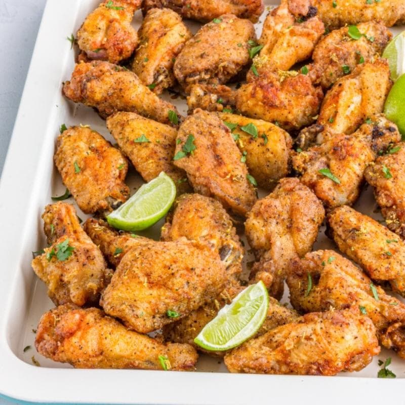 Cooked Lemon Pepper Wings on a baking sheet with lime wedges