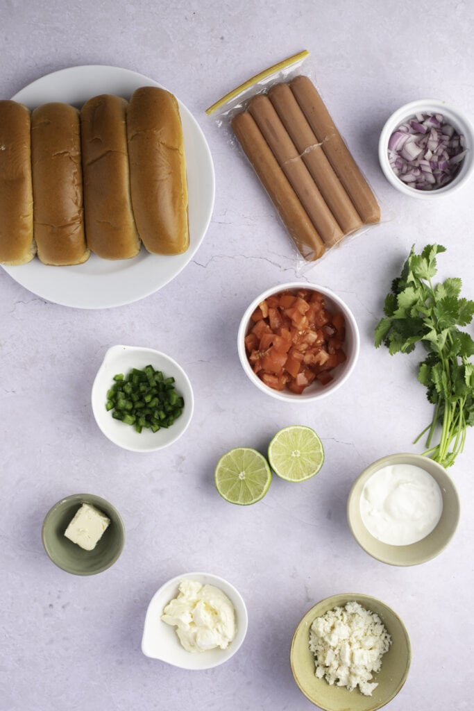 Mexican Hot Dogs Ingredients: sausages, tomatoes, lime juice, red onion, cilantro, scallions, sour cream, and bread buns
