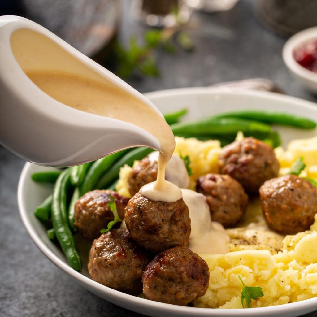Pouring Gravy into Meatballs with Mashed Potatoes and Green Beans