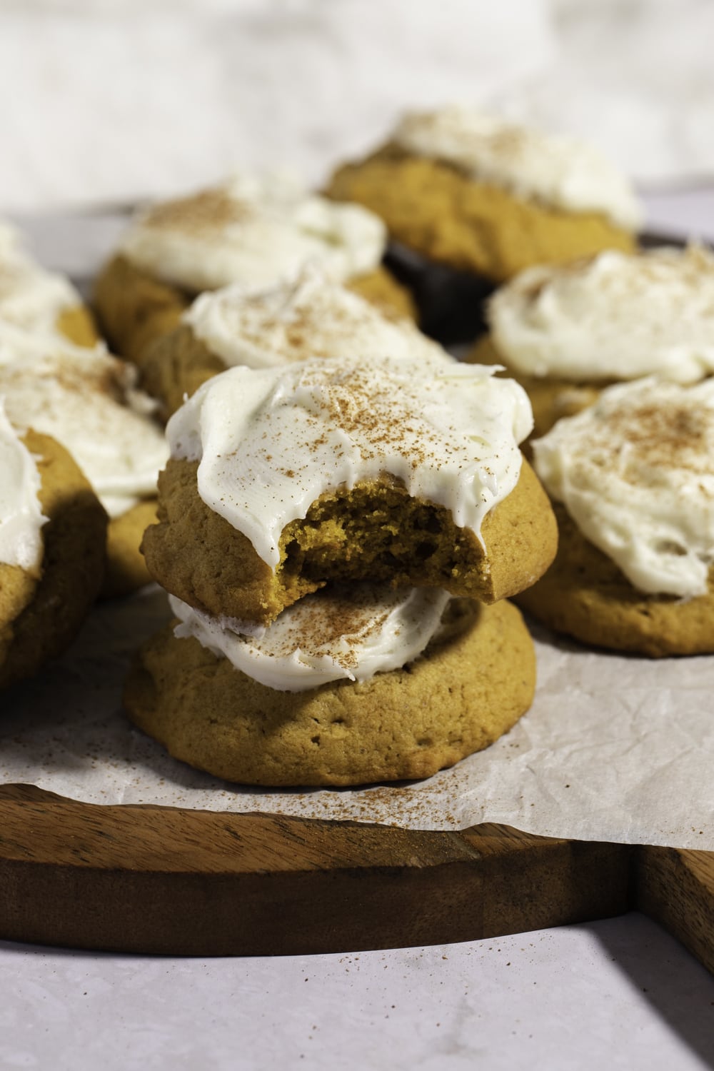 Pumpkin cookies with cream cheese frosting stack on a wooden board. 